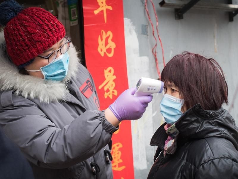 Eine Gemeindemitarbeiterin misst die Körpertemperatur einer Passantin in der Nähe der Kranichpagode in Wuhan. Foto: Xiao Yijiu/XinHua/dpa