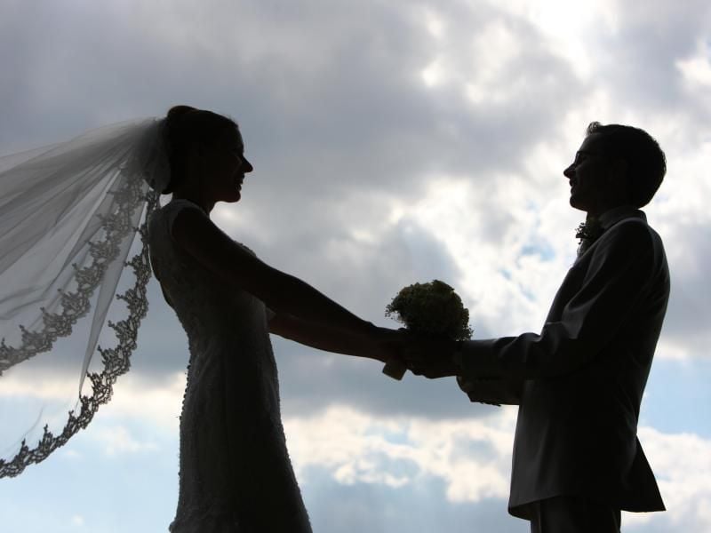 Die Silhouette eines frisch vermählten Hochzeitspaares zeichnet sich im Gegenlicht ab. Foto: Patrick Pleul/zb/dpa/Illustration