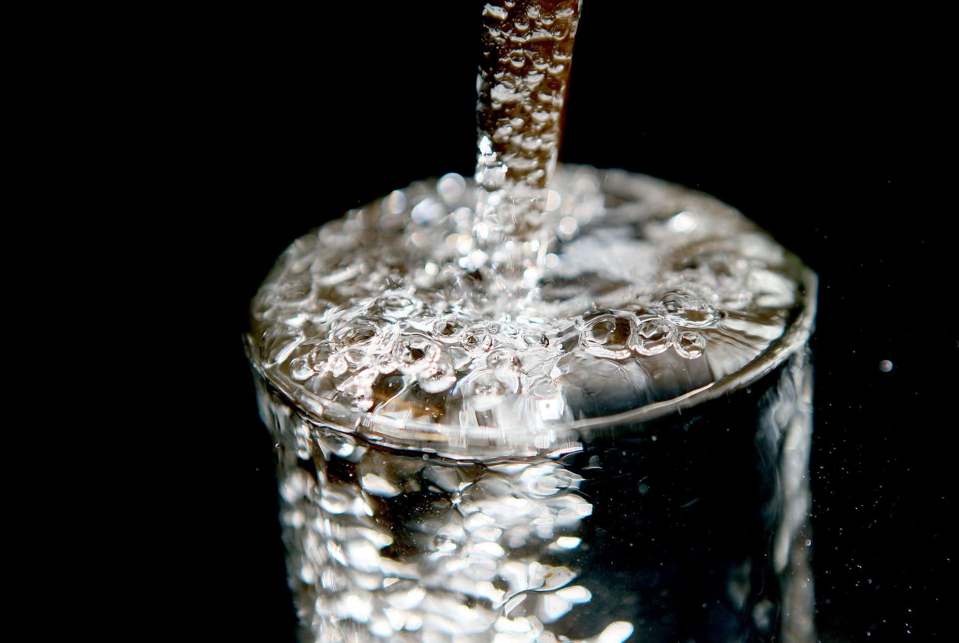 Ein überlaufendes Glas, in das Trinkwasser läuft. Sauberes Wasser wird in Zukunft noch wertvoller.