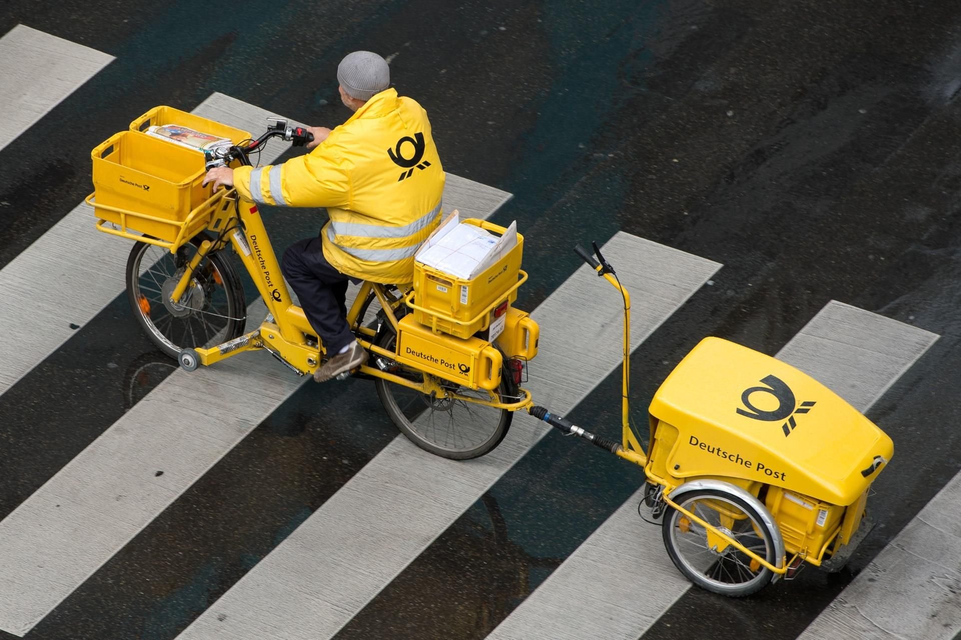 Ein Briefträger der Deutschen Post fährt mit einem Fahrrad (E-Bike) über einen Zebrastreifen.