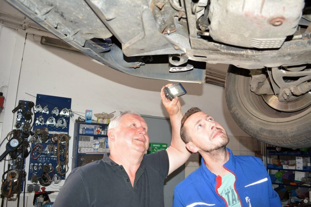 Wolfram Schiel und sein Sohn Michael schauen unter ein Auto, das repariert werden soll.
