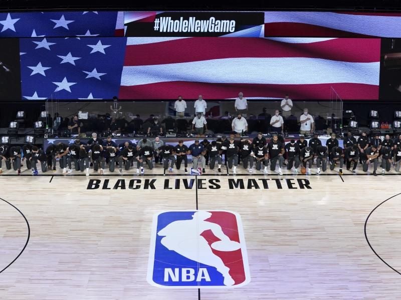 Die Spieler der New Orleans Pelicans und Utah Jazz knien bei der Nationalhymne gemeinsam vor einem „Black Lives Matter”-Schriftzug. Foto: Ashley Landis/Pool AP/dpa