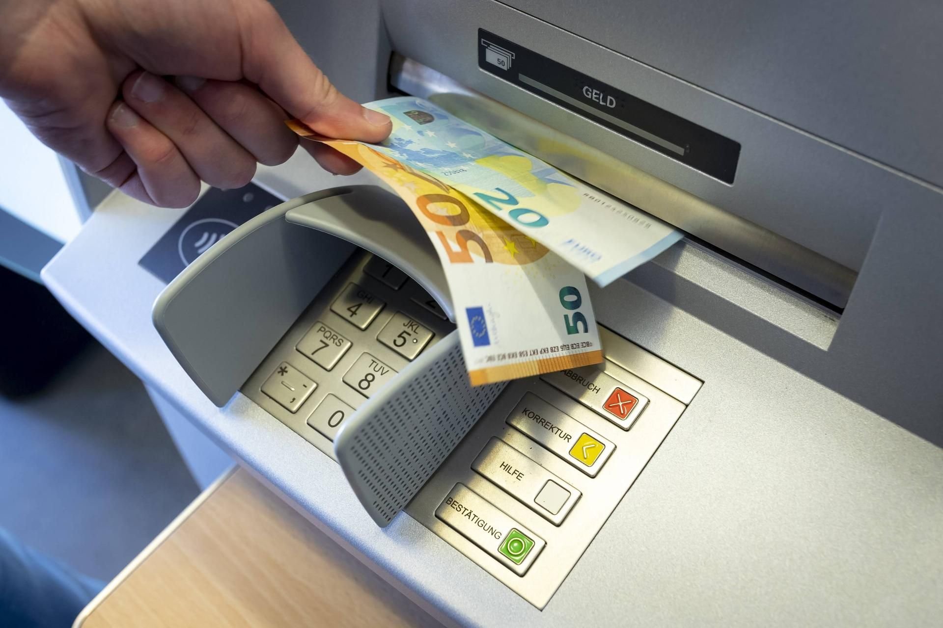 Ein Mann zieht Geldscheine aus dem Ausgabeschacht eines Bankautomaten.