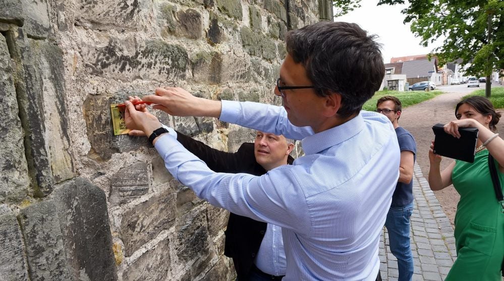 Akens evangelischer Pfarrer Georg Neugebauer (vorn) und Klaus-Martin Bresgott vom Kulturbüro des Rates der EKD befestigen die „LandGut“-Plakette an der Mauer der Nikolaikirche.