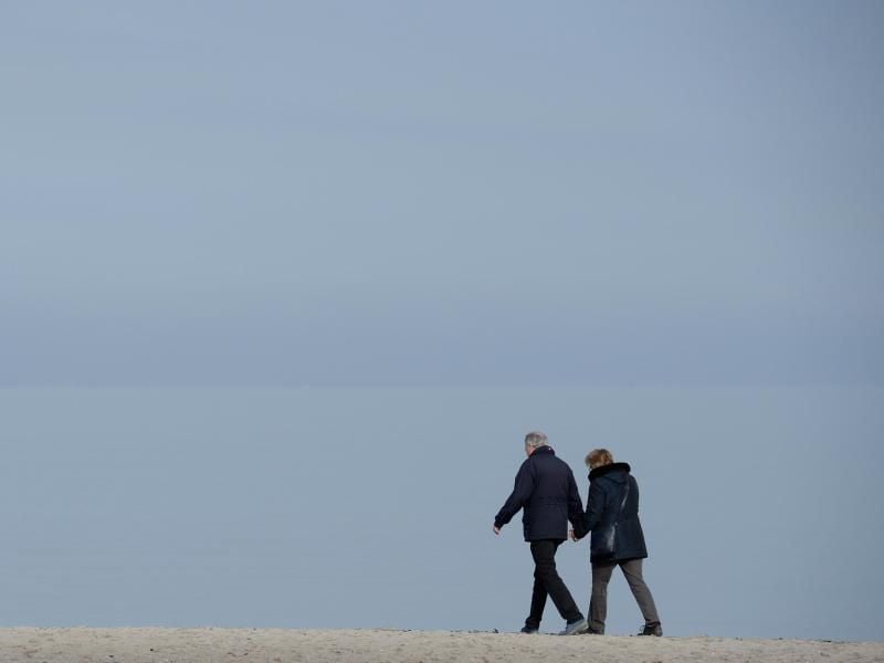 Ein Paar geht in Lübeck-Travemünde (Schleswig-Holstein) bei blauem Himmel am Strand entlang. Foto: Daniel Reinhardt/Archiv