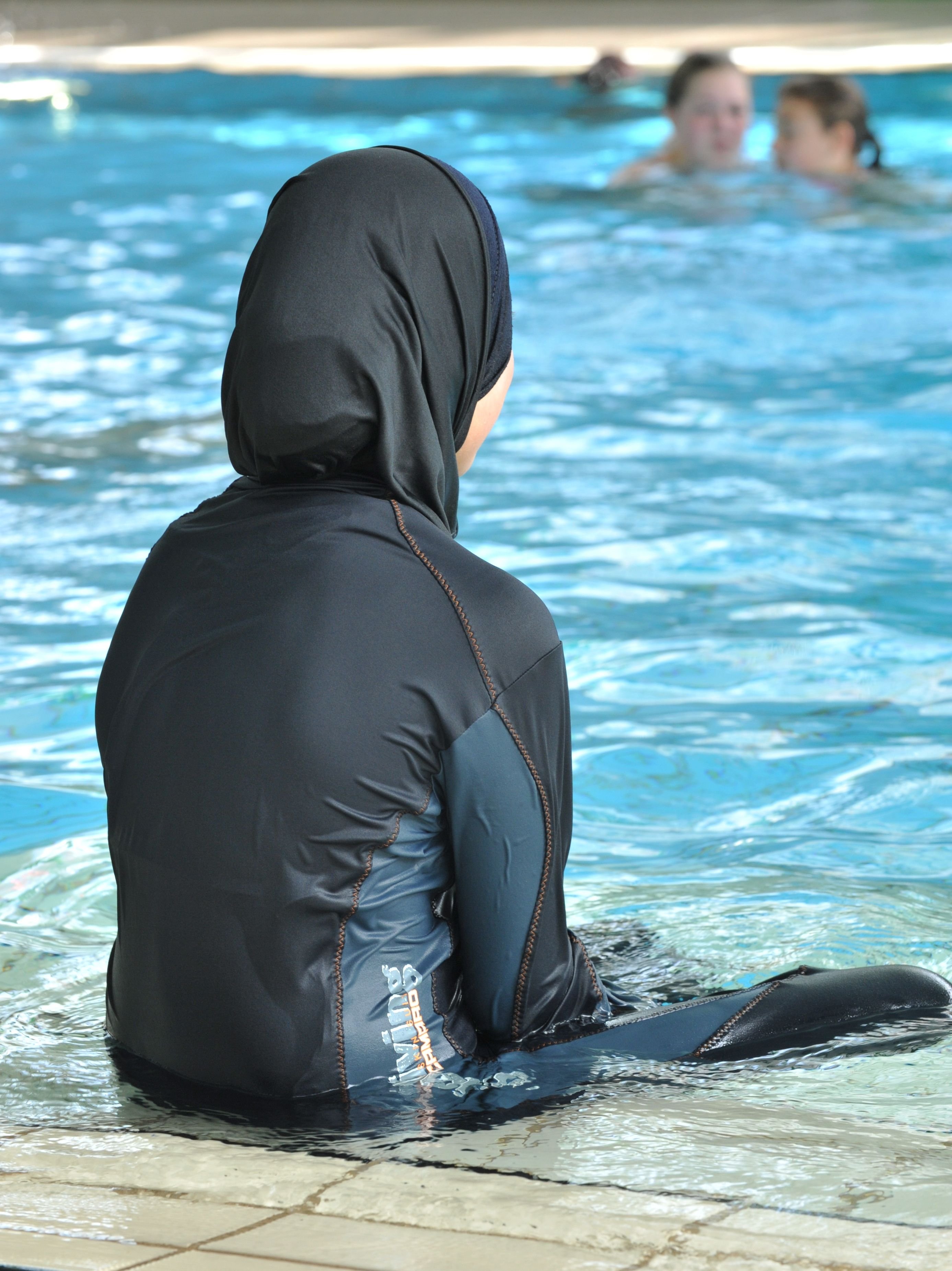 Eine Muslima sitzt mit einem Burkini bekleidet an einem Schwimmbecken.