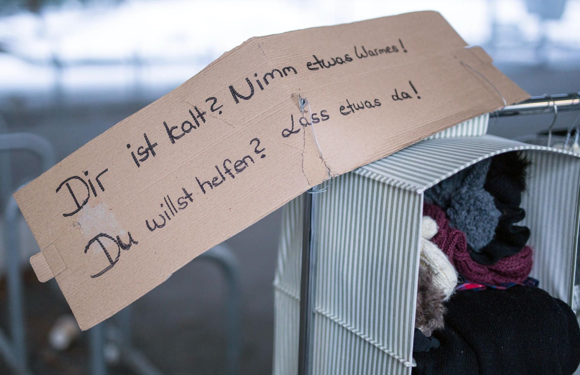 Ein Schild mit der Aufschrift "Dir ist kalt? Nimm etwas warmes! Du willt helfen? Lass etwas da!" ruft in Stuttgart an einem Kleiderständer zum Geben und Nehmen von Winterkleidung auf.