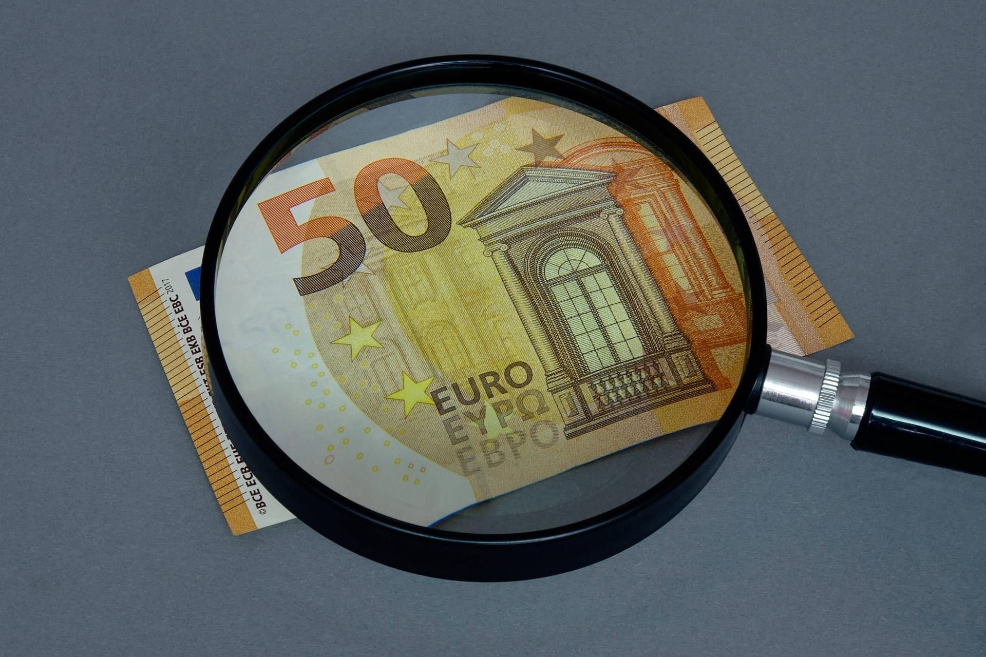 Echt oder Falschgeld? Eine Lupe liegt über einem Geldschein.