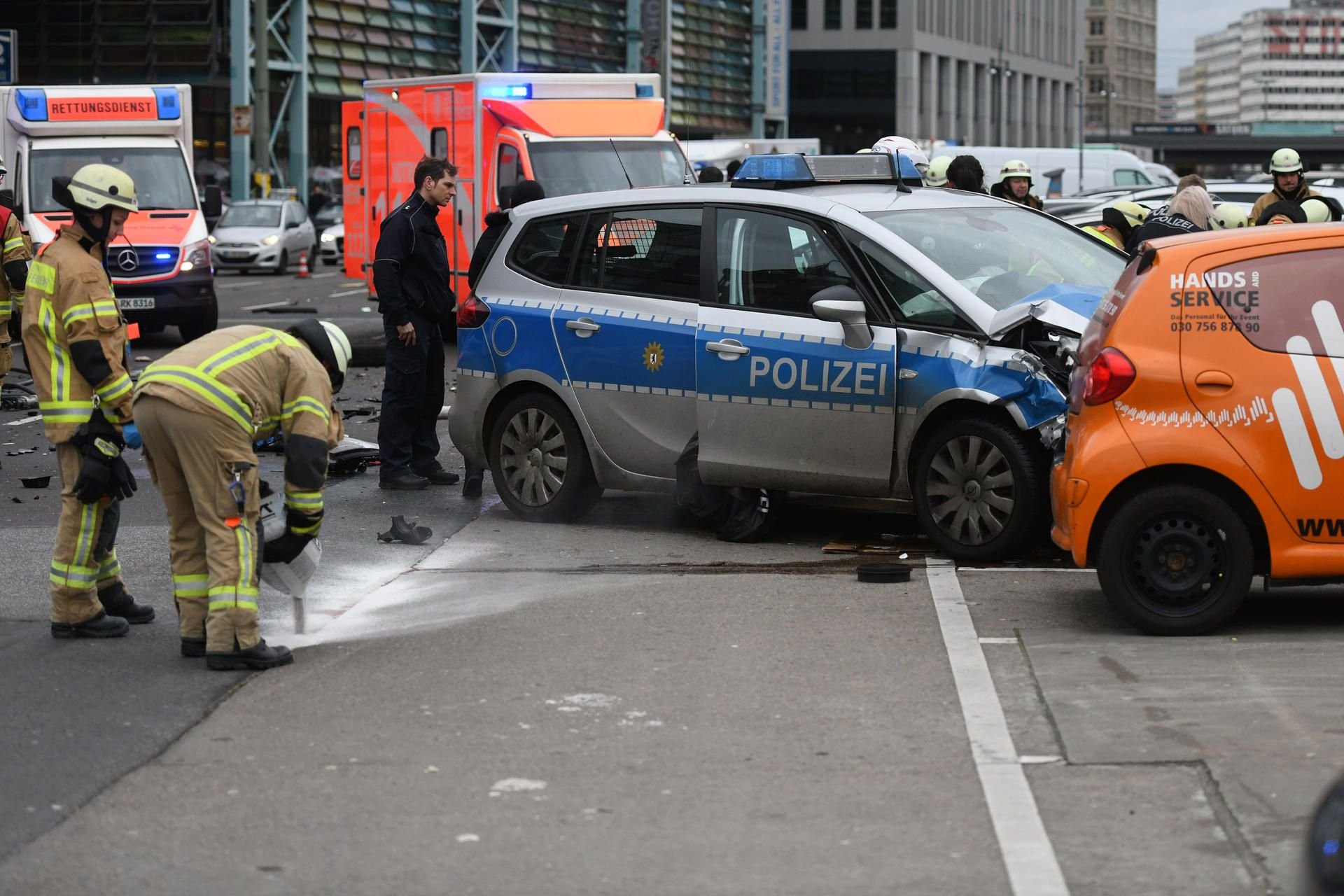 Polizisten und Feuerwehrmänner am Unfallort in Berlin, an dem ein Polizeifahrzeug während eines Einsatzes mit einem weiteren Auto zusammenprallte.