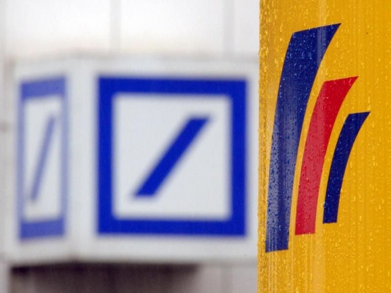 Das Logo der Deutschen Bank (l.) hinter dem Logo der Postbank. Foto: Federico Gambarini/Archivbild