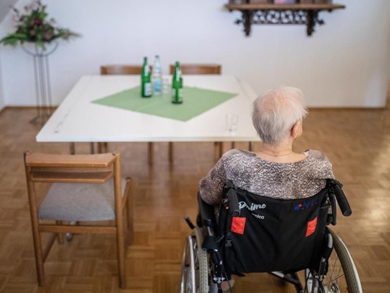 Eine ältere Frau sitzt in einem Pflegeheim in ihrem Rollstuhl vor einem Tisch. Foto: Marcel Kusch/dpa
