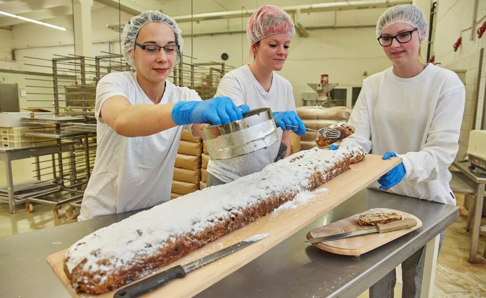 Mitarbeiter der Wohlgemuth Süßwaren GmbH in Bernburg bezuckern ein Stück des aus Dresden angelieferten Riesenstollen.