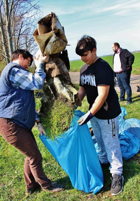 Michaela Lange und Ferenc Frank verfrachten einen Teppich, auf dem sogar schon Gras wächst, in einen Müllsack.