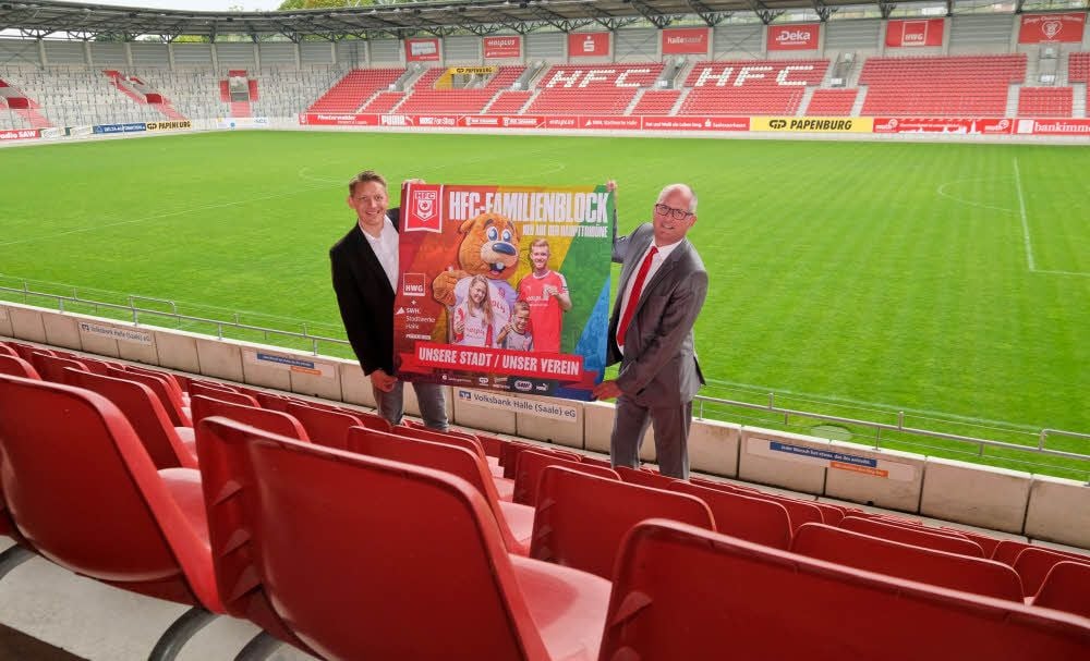 Sebastian Rose (links) und Jens Rauschenbach zeigen das neue Werbeplakat für den Familienblock im Erdgas Sportpark.