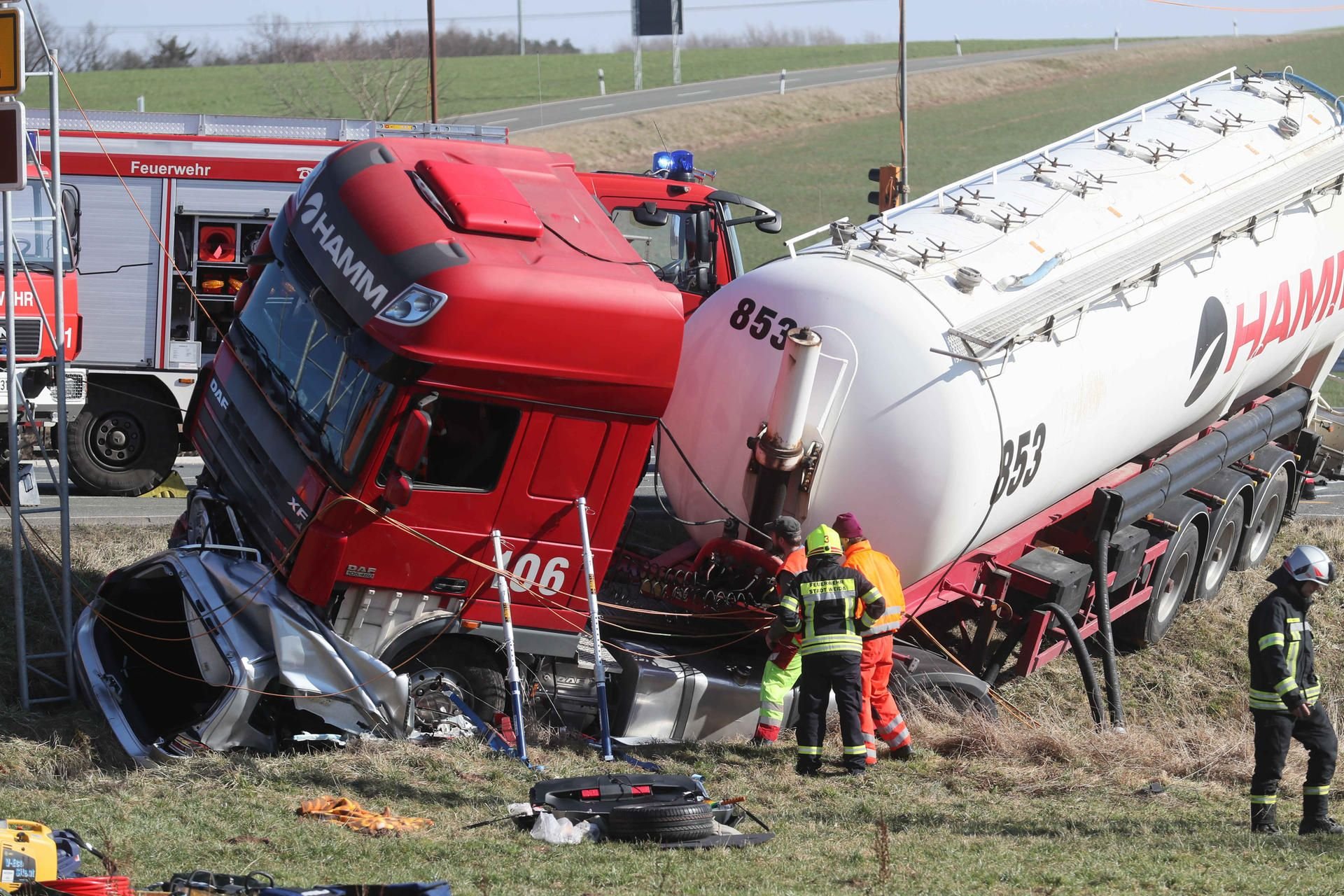 Feuerwehrleute stehen auf der B92 bei Weida neben einem Lkw, der einen Pkw unter sich begraben hat.