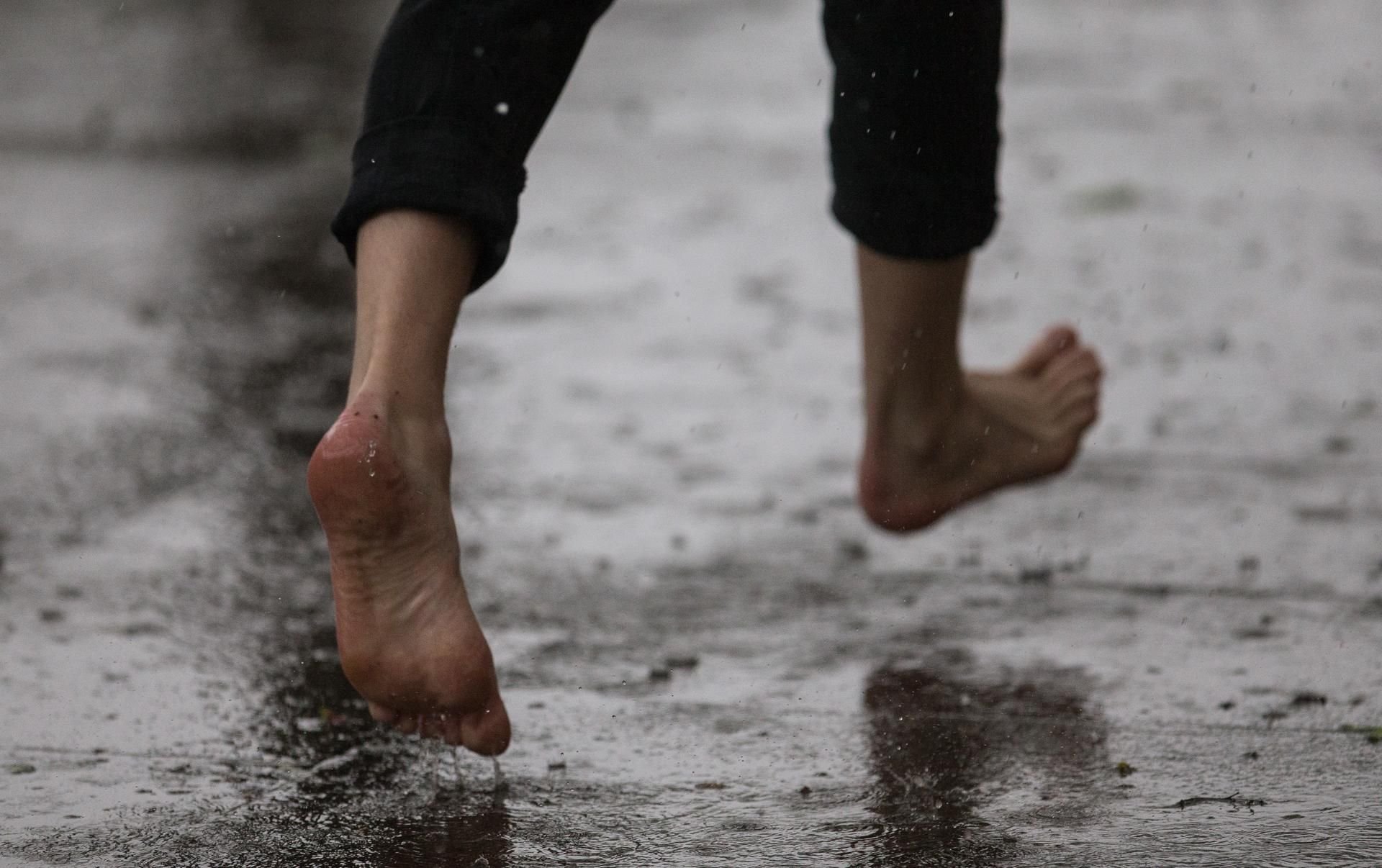 Jemand läuft barfuß durch den Regen. (Symbolbild)