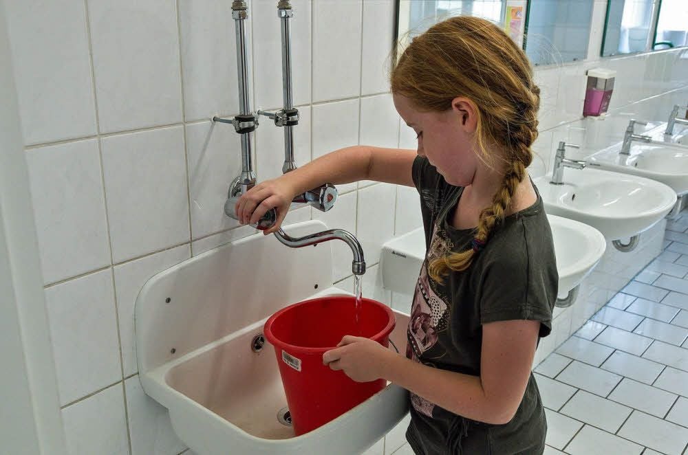 Lena füllt den Eimer mit Wasser, damit die Tafel im Klassenzimmer geputzt werden kann.