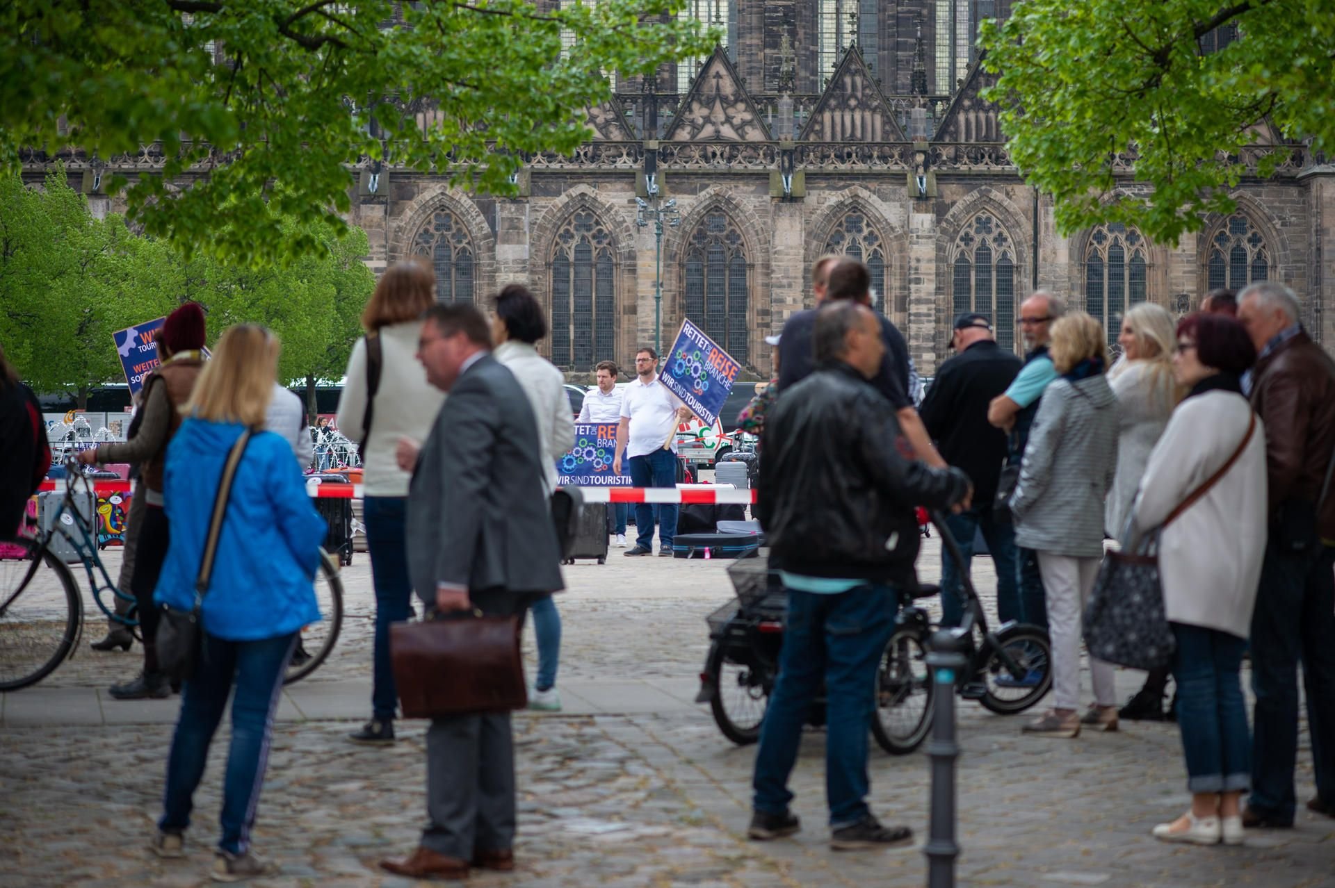 "Rettet die Reisebranche" und "Wir sind Touristik" steht auf einem Schild eines Demonstranten, der hinter einer Absperrung auf dem Domplatz steht.