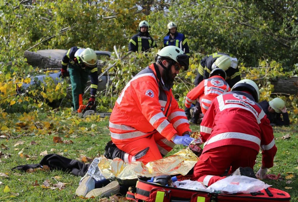 Rettungskräfte kümmern sich um die „Verletzten“ in Gollma. Im Hintergrund befreit die Feuerwehr ein Auto, das unter einem Baum liegt.