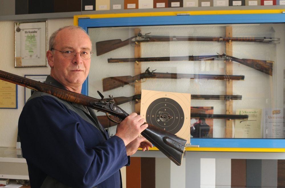 Der Hassenhausener Maik Kirste steht mit der von ihm gebauten „Lancaster 1770“ vor einem Schrank mit weiteren von ihm angefertigten Nachbildungen historischer Gewehre.