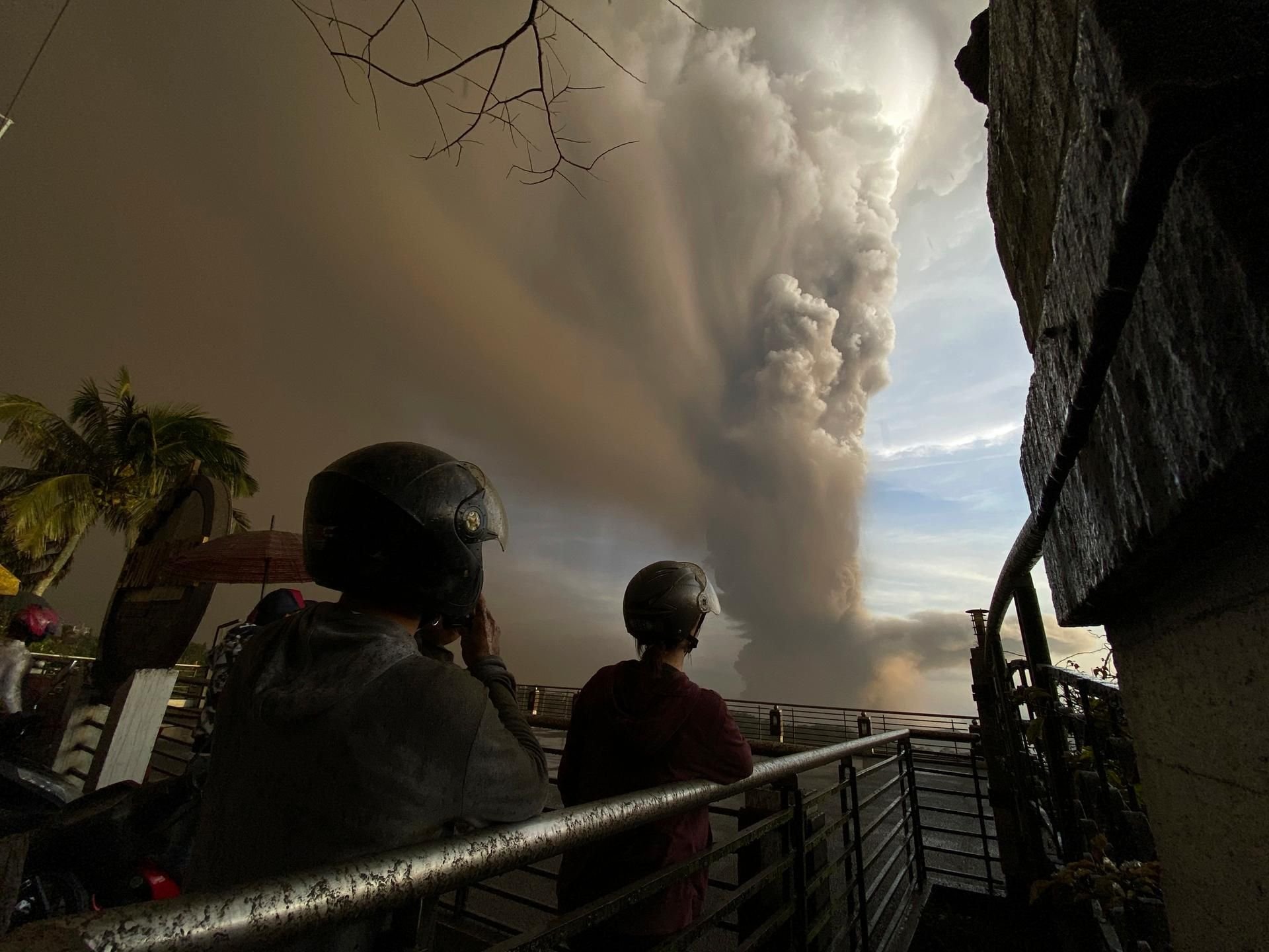 Menschen beobachten auf einer Brücke riesige Rauchwolken, die während eines Ausbruchs des Vulkans Taal in die Luft steigen.