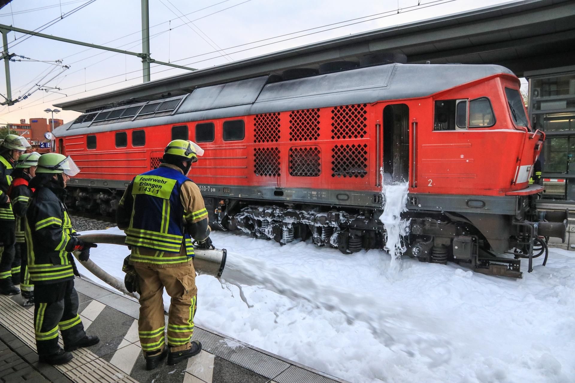 Einsatzkräfte der Feuerwehr Erlangen löschen mit Löschschaum die Diesellok eines Güterzuges.