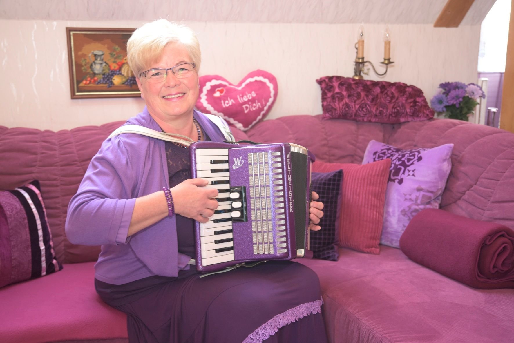 Frau Lila sitzt auf ihrem lila Sofa in ihrem lila Wohnzimmer und spielt auf einem lila Akkordeon.