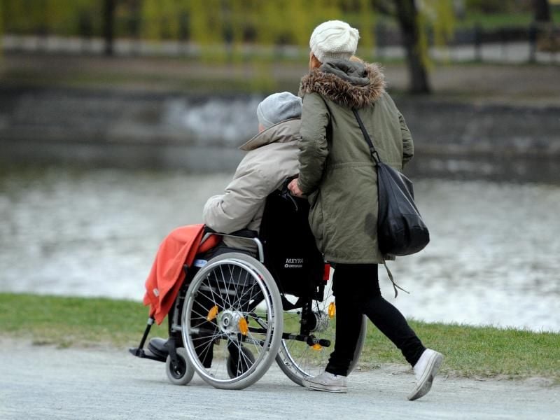 Eine junge Frau schiebt eine Frau in einem Rollstuhl am Landwehrkanal entlang. Foto: Britta Pedersen/Archiv