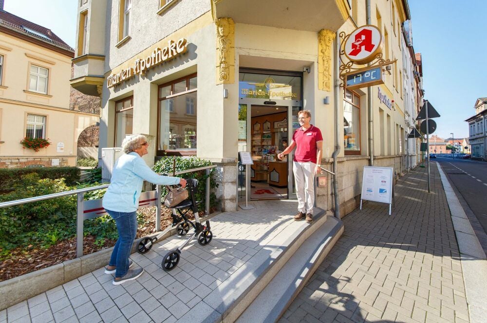 Apothekeninhaber Curt Wenzel begrüßt seine Kundin Rita Ehret, die sich freut, dass ihr die Rampe den Zugang mit dem Rollator erleichtert.