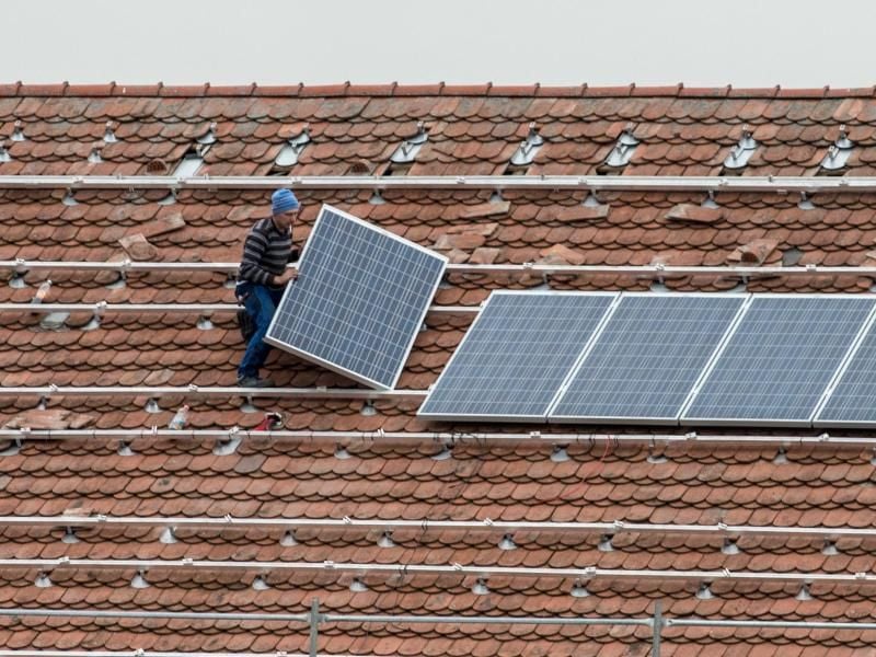 Ein Arbeiter montiert ein Solarmodul auf ein Dach. Foto: Armin Weigel/Archiv