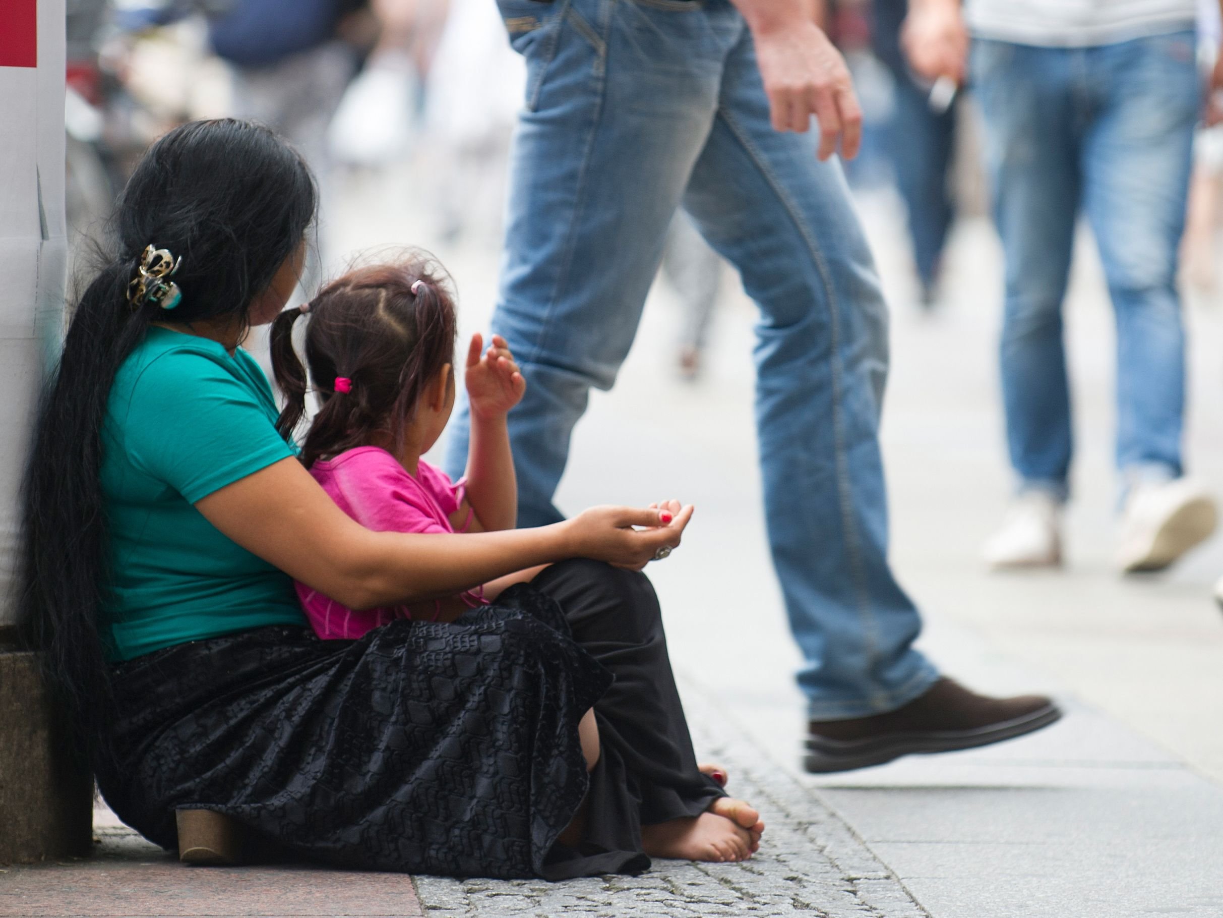 Eine Frau und ein Kind sitzen auf einem Bürgersteig und betteln um Geld.