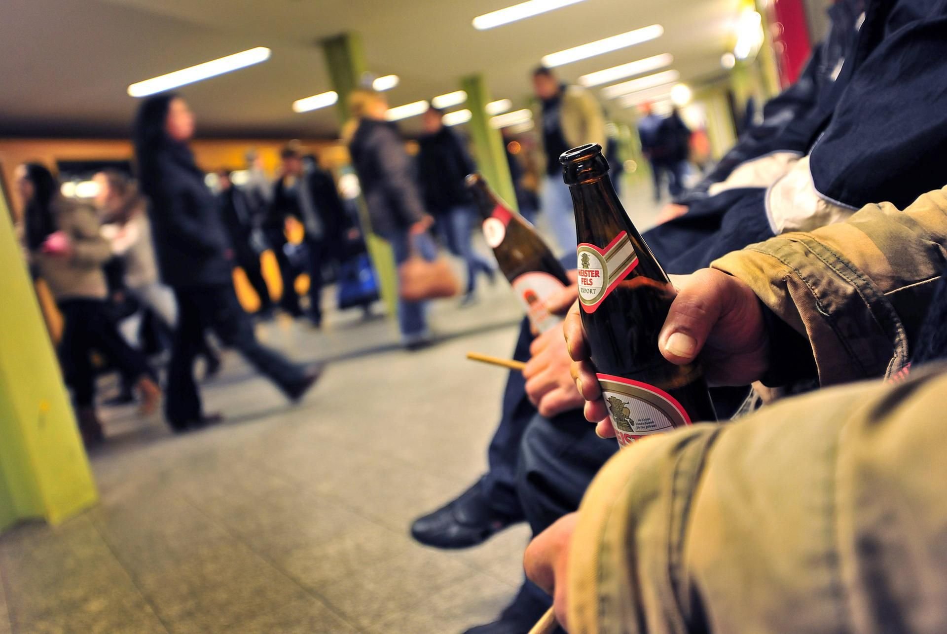 Männer mit Bierflaschen sitzen an einer Haltestelle.