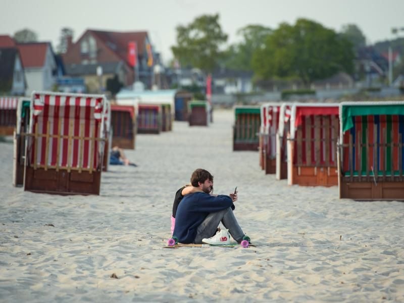 Ein Paar sitzt im Sand vor geschlossenen Strandkörben. Foto: Gregor Fischer/dpa
