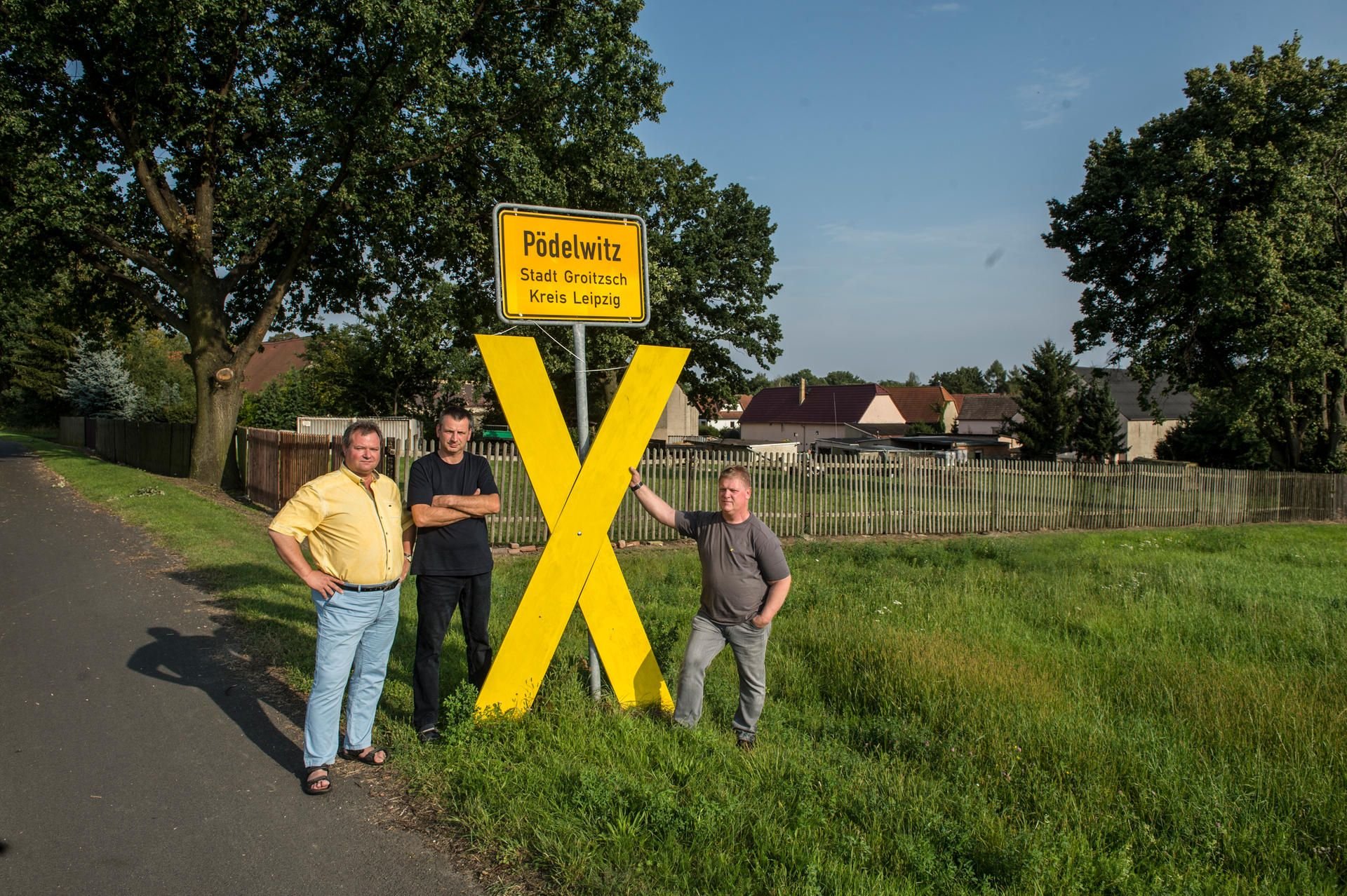 Sie wollen den Baggern nicht weichen: Die Pödelwitzer Thilo Kraneis, André Kremkow und Jens Hausner (v.l.) an einem gelben Andreaskreuz, das den Widerstand bis zum Tag X symbolisiert.
