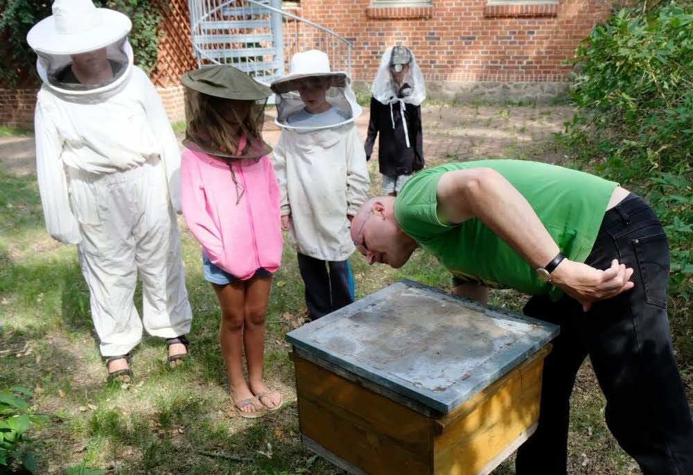 Pfarrer und Hobby-Imker Hans-Jörg Heinze erklärt den Kindern den Aufbau einer Bienenkiste und gewährt anschließend Einblicke.
