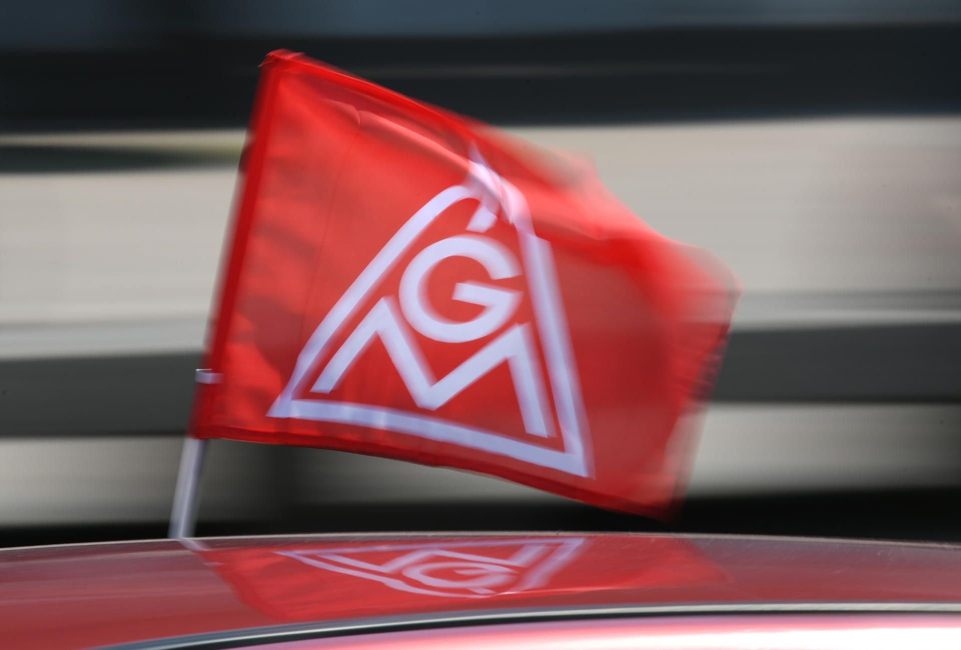 Eine rote IG-Metall-Flagge spiegelt sich in einem Fahrzeugdach.