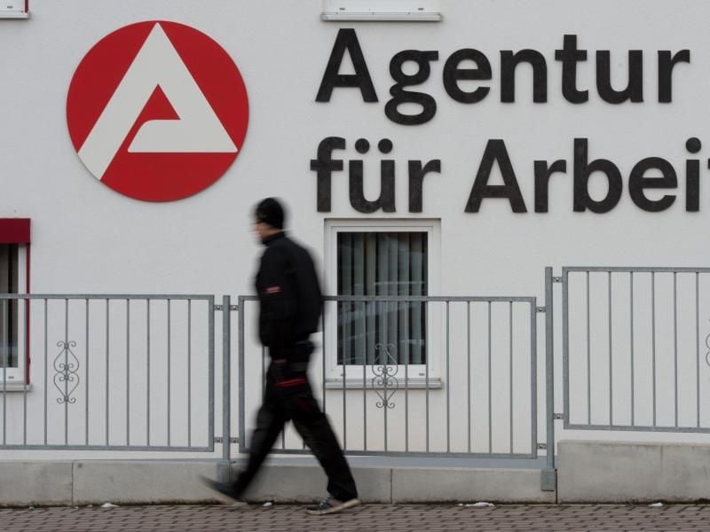 Ein Mann geht an dem Logo der Agentur für Arbeit vorbei. Foto: Sebastian Kahnert/dpa-Zentralbild/dpa/Symbolbild