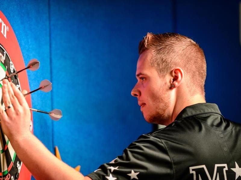 Dartspieler Max Hopp zieht seine Pfeile aus der Scheibe. Foto: Thomas Eisenhuth/Archiv