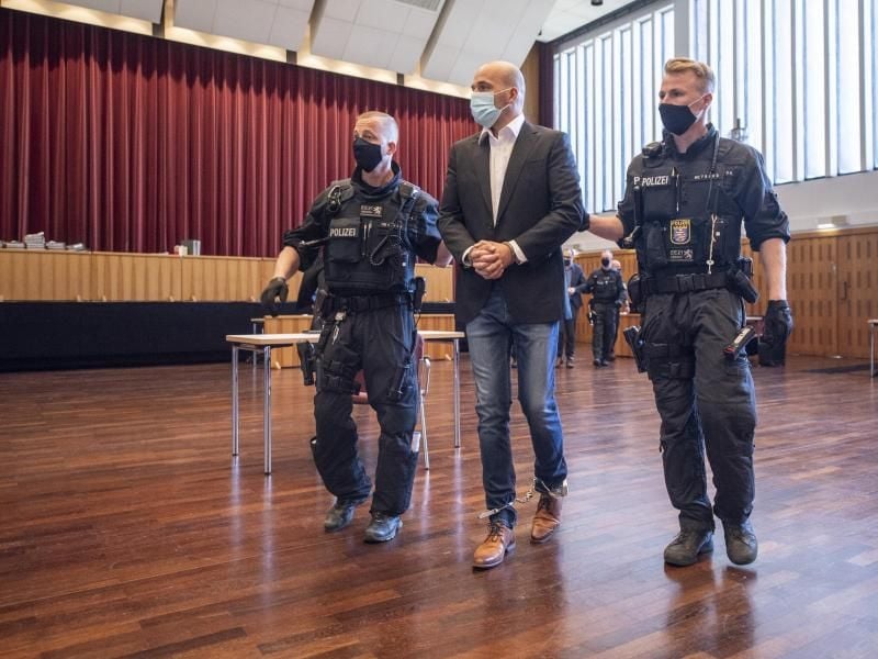 An Händen und Füßen gefesselt ist einer der Hauptangeklagten, den bewaffnete Polizisten in die zu einem Gerichtssaal umfunktionierte Kongresshalle in Gießen bringen. Foto: Boris Roessler/dpa