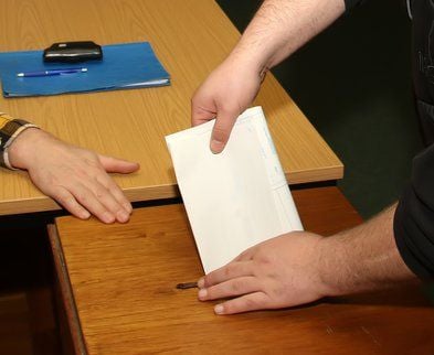 Ein Mann steckt einen Stimmzettel in eine Wahlurne