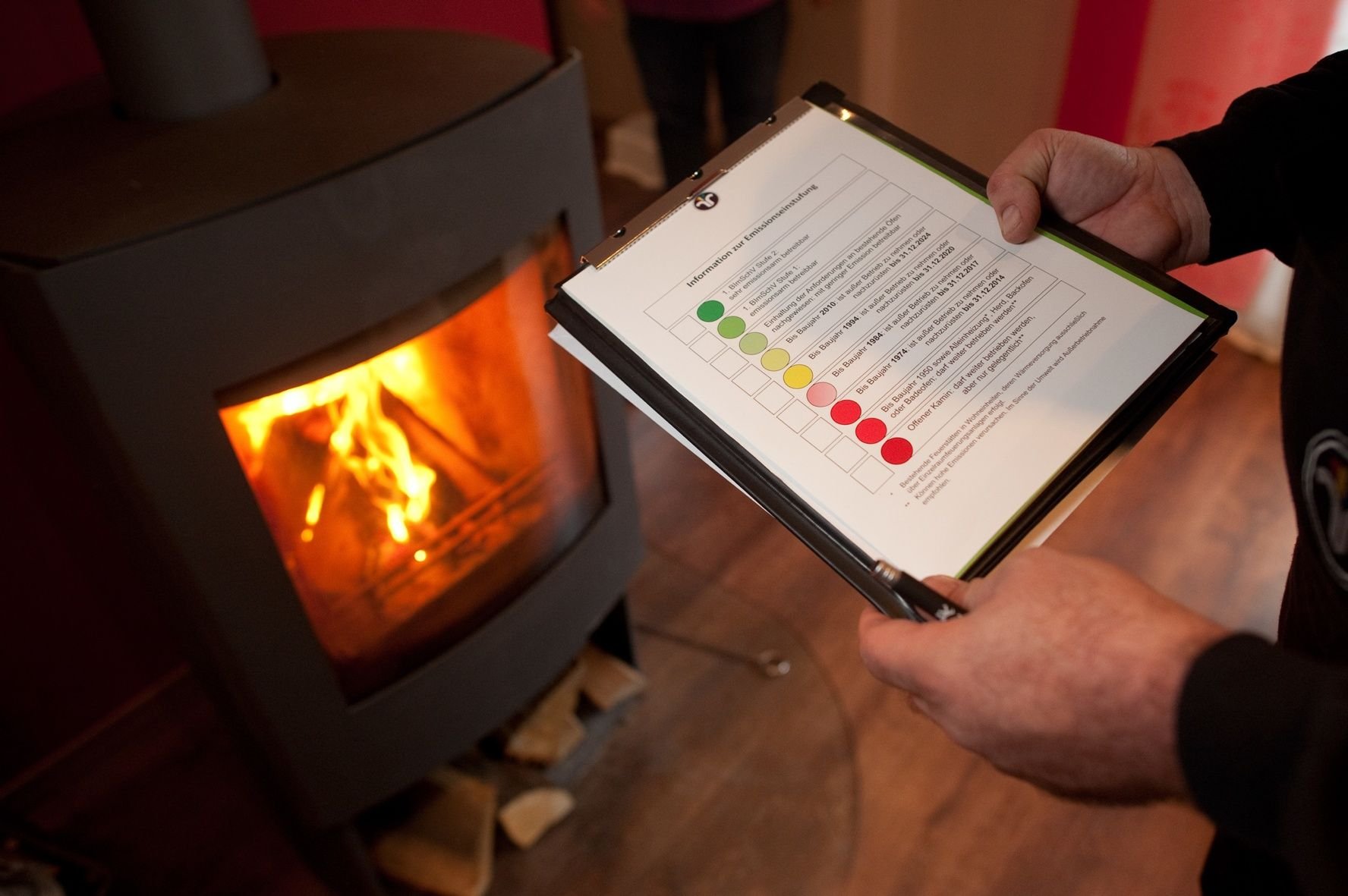 Ein Bezirksschornsteinfeger stuft während einer Feuerstättenschau den Emissionsausstoß eines Kaminofens mit Hilfe einer Tabelle ein.