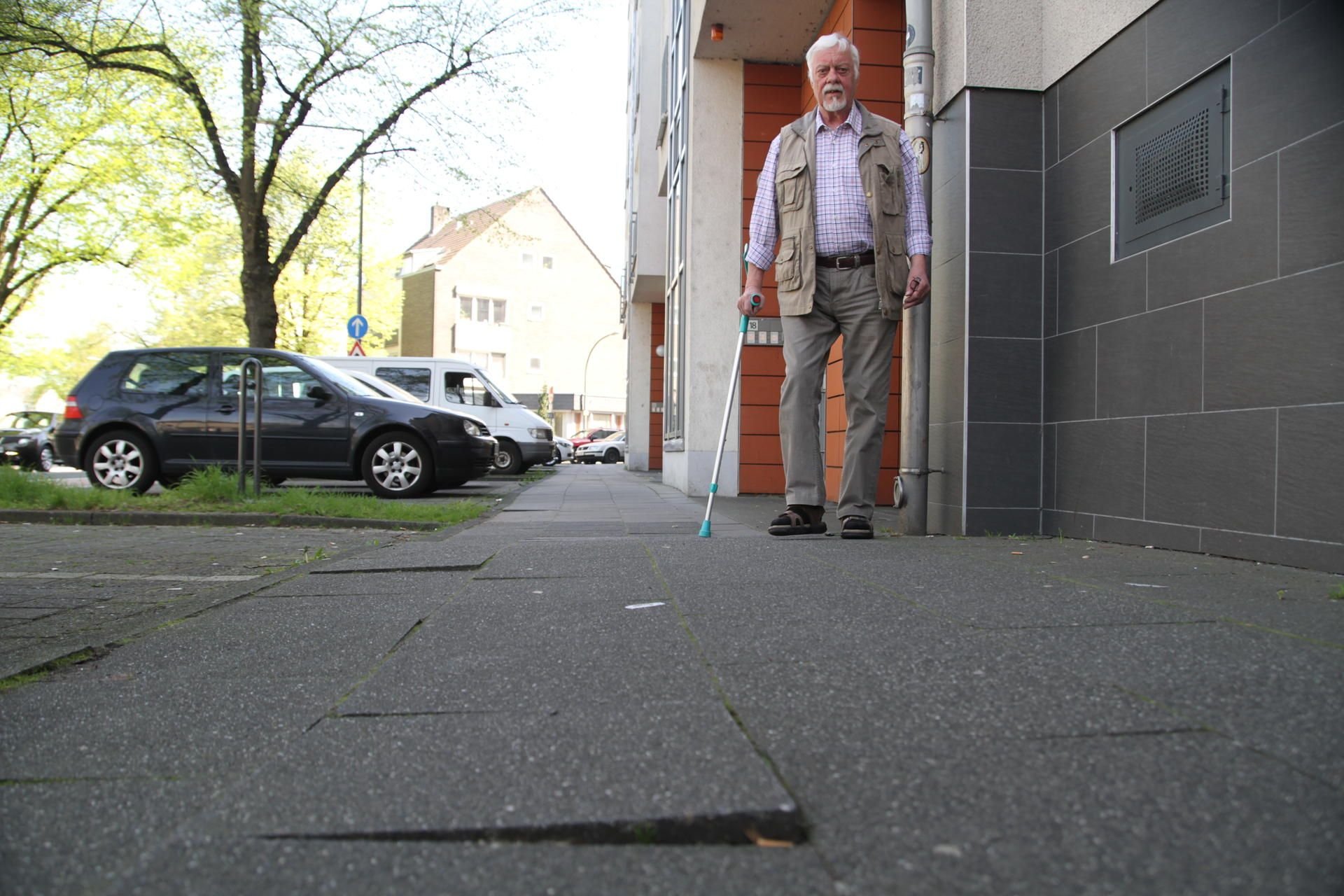 Arno Krämer zeigt mit seiner Krücke auf den Unfallort in Köln, wo Gehwegplatten lose sind.