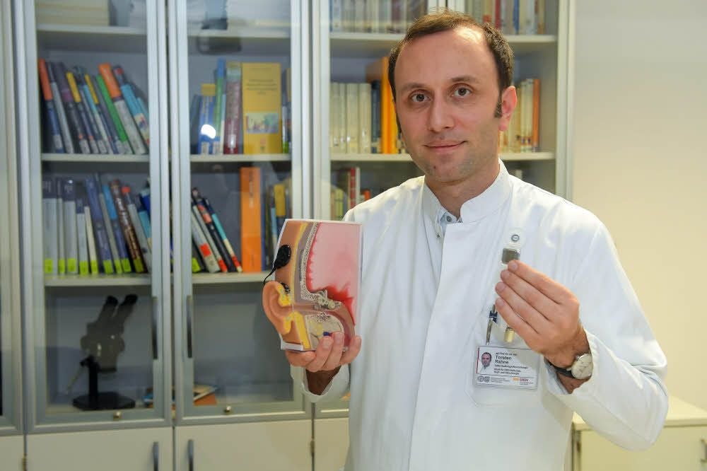 Prof. Torsten Rahne, Leiter der Audiologie am UKH, hält ein Cochlea-Implantat in den Händen.