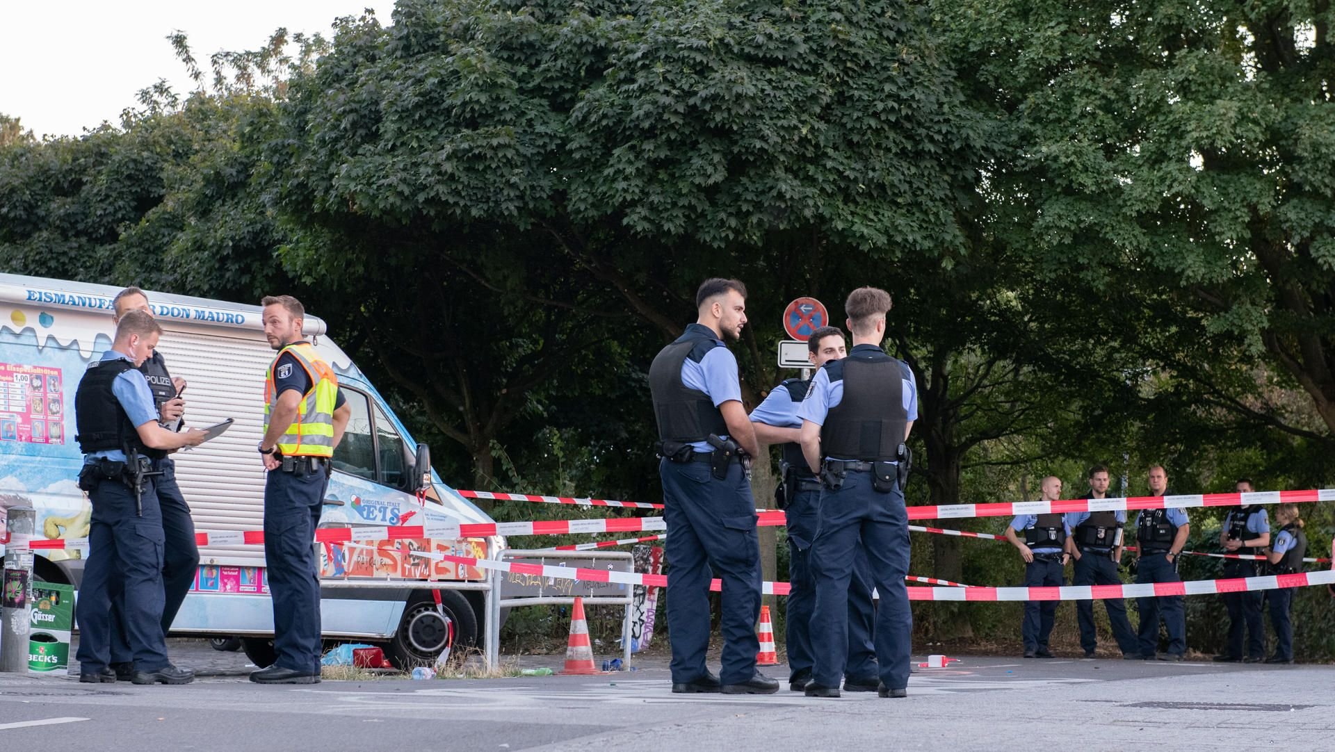 Polizisten stehen an einem abgesperrten Bereich an einem Zugang zum Tempelhofer Feld an der Oderstraße. Dort wurde ein Mann durch Schüsse lebensgefährlich verletzt.