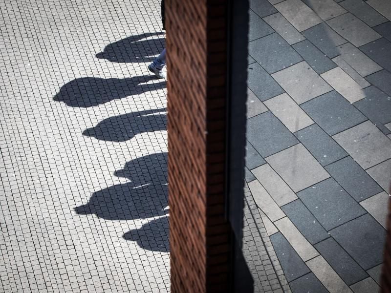Die Mittagssonne wirft Schatten von Menschen auf das Betonpflaster. Foto: Frank Rumpenhorst/Archiv