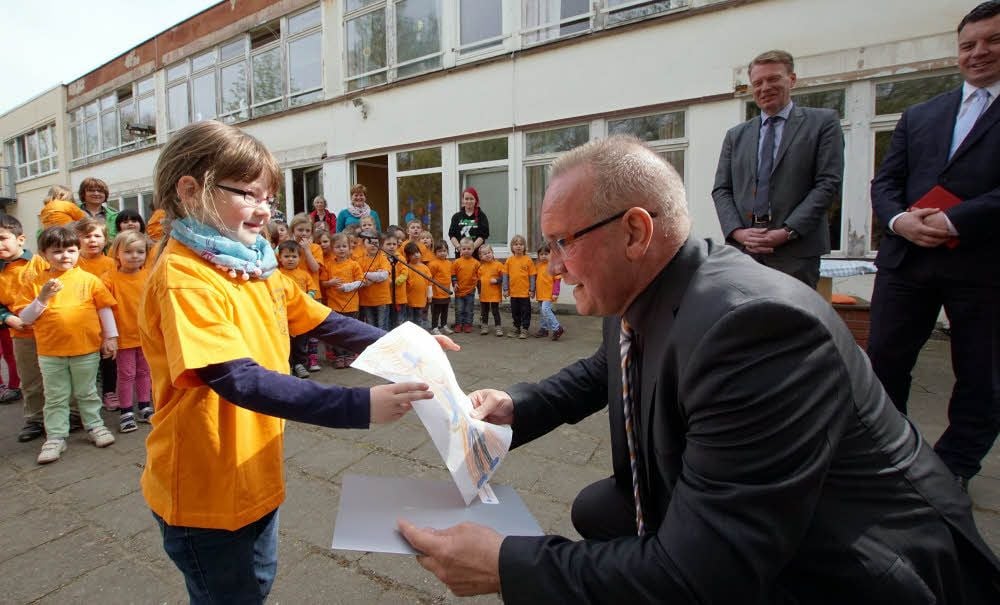 Finanzminister André Schröder (h.r.) hat in der Kindertagesstätte Süderstadt den Fördermittelbescheid für die energetische Sanierung der Einrichtung übergeben. Melanie nutzt das, um Oberbürgermeister Frank Ruch ein Bild zu schenken, auf dem sie den OB gemalt hat.