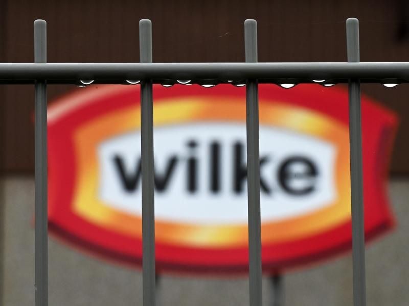 Wassertropfen hängen am Zaun vor dem Logo des nordhessischen Wurstherstellers Wilke. Foto: Uwe Zucchi/dpa/Archivbild