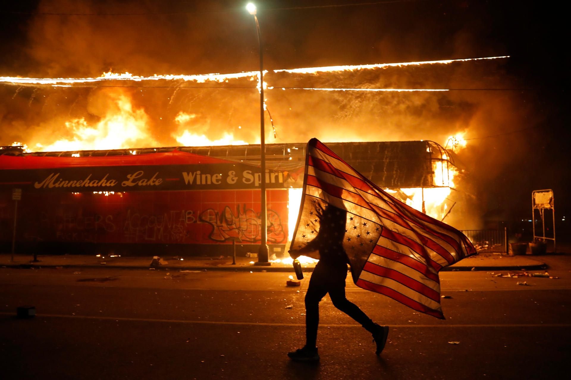 Ein Demonstrant trägt neben einem brennenden Gebäude eine US-Flagge während der Proteste nach dem Tod von George Floyd, der in Folge einer brutalen Festnahme durch einen Polizisten in Minneapolis starb.