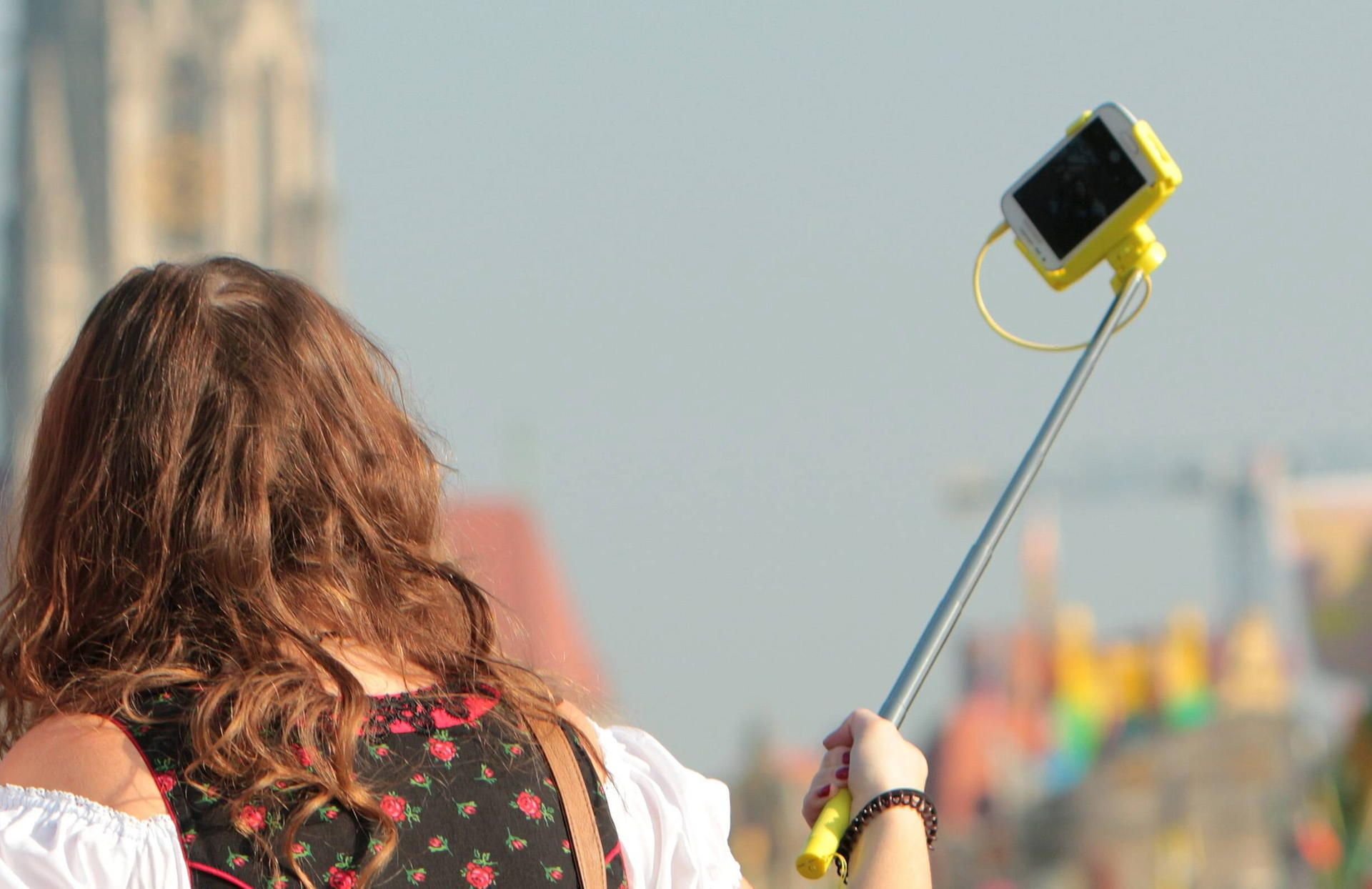Eine junges Mädchen macht mit Selfiestick und Smartphone eine Aufnahme von sich.