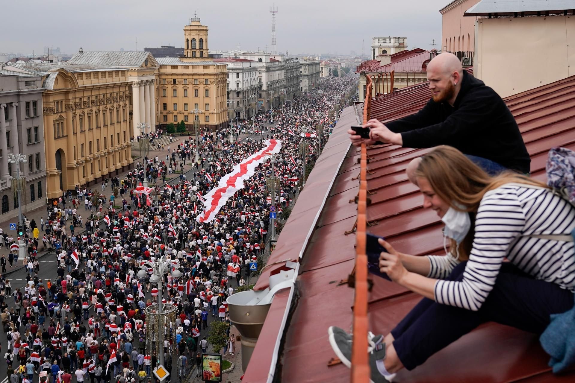 Menschen beobachten von einem Dach aus den großen Demonstrationszug in Minsk.